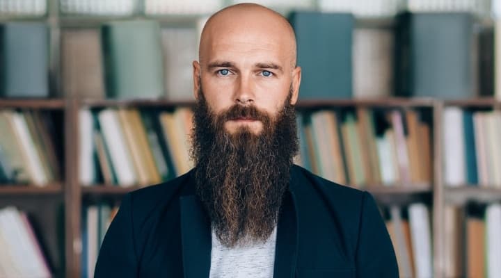 Portrait of a bearded man standing in front of a bookshelf