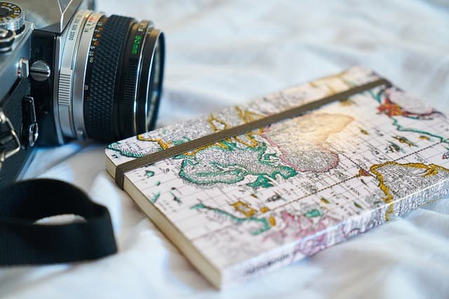 A film camera beside a notebook printed with an antique world map