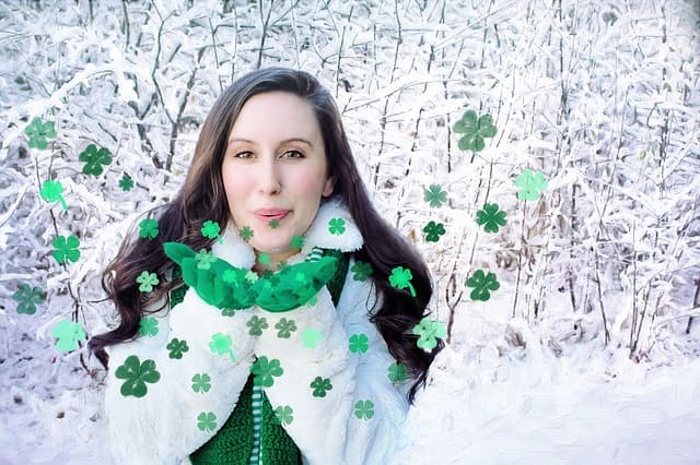A person in a white coat blowing green paper shamrocks in a snowy wood