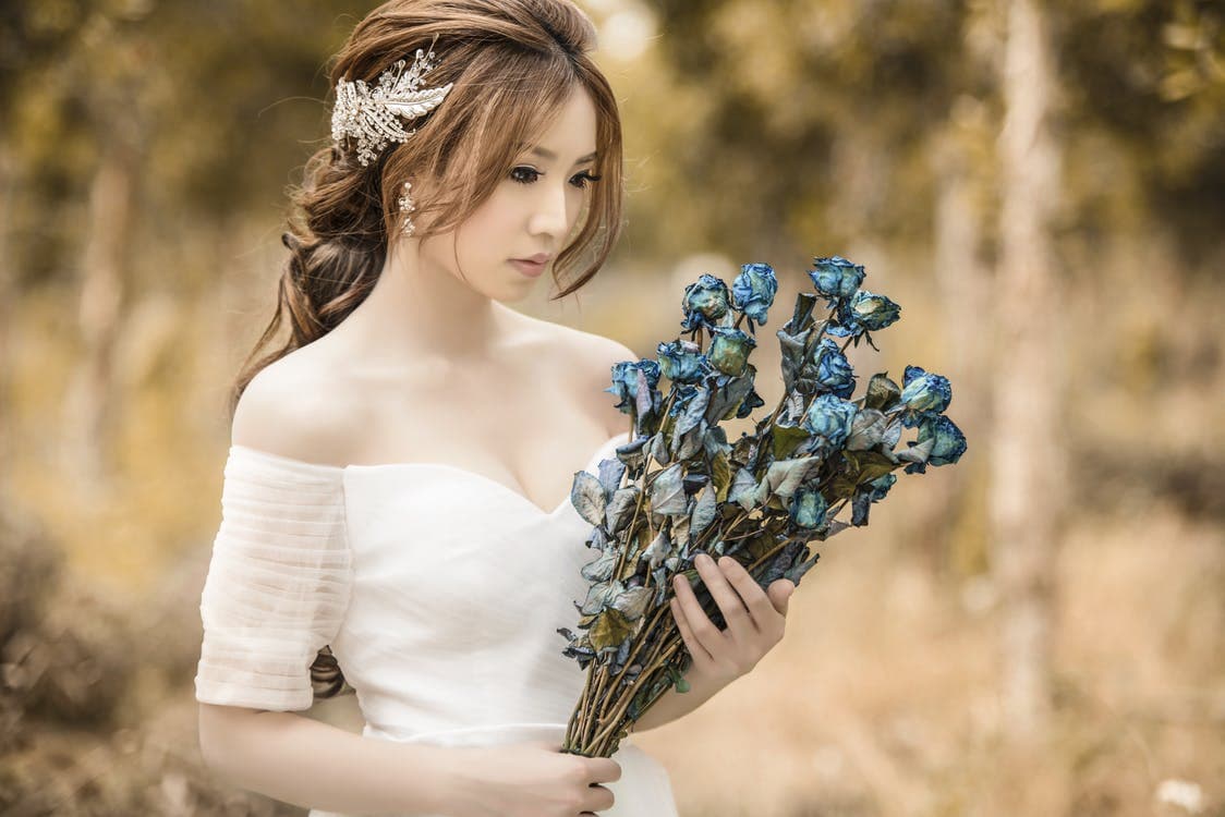 A bride in a white dress holding a bouquet of dried blue roses