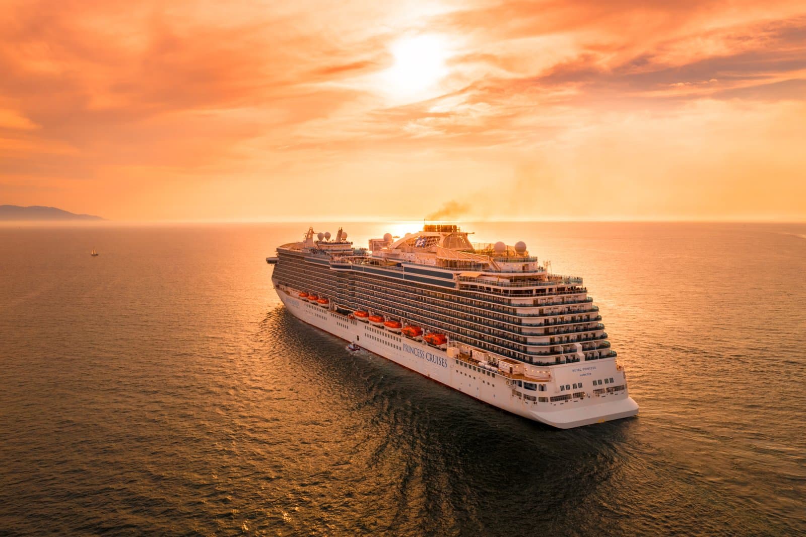 A large cruise ship at sea under an orange sunset sky