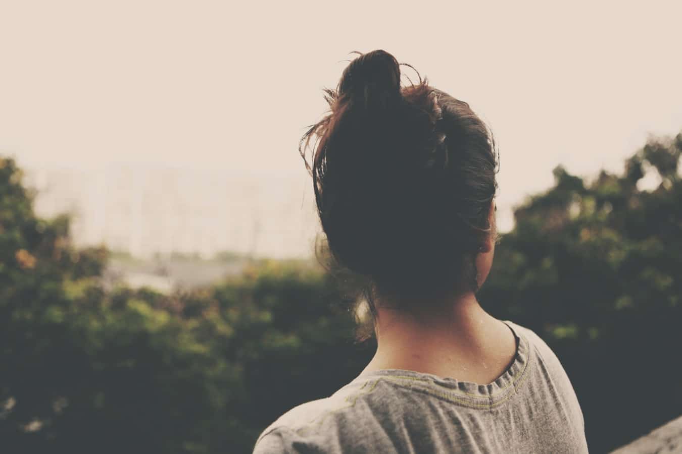 Back view of a person looking out over treetops and open sky